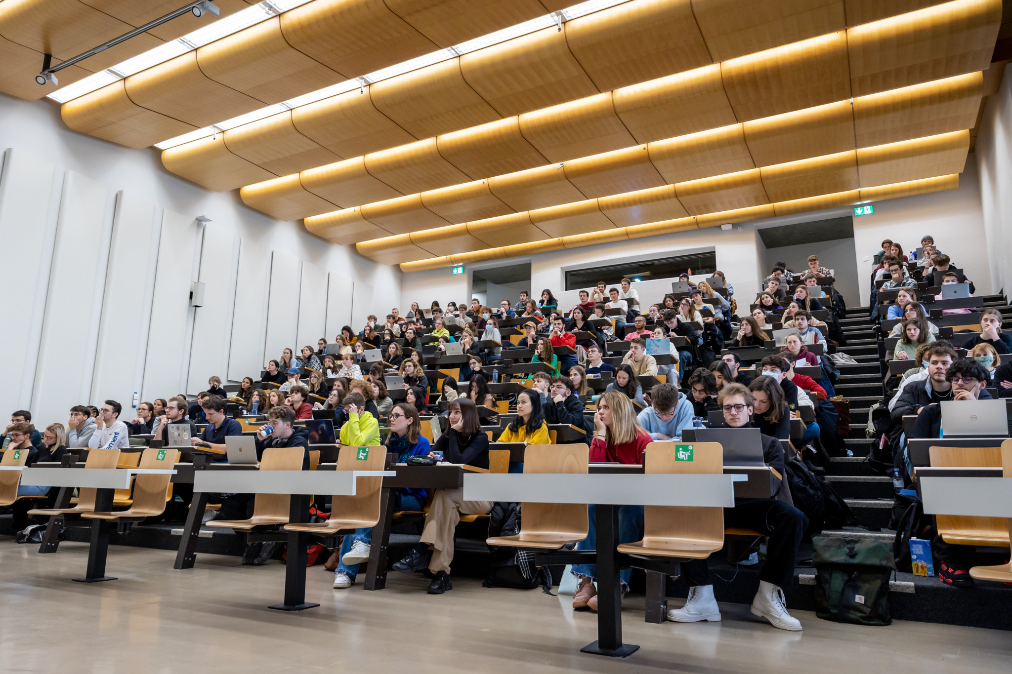 Étudiants assis dans un grand amphithéâtre sur le campus de l’EPFL, travaillant sur des ordinateurs portables, le 22 février 2022.