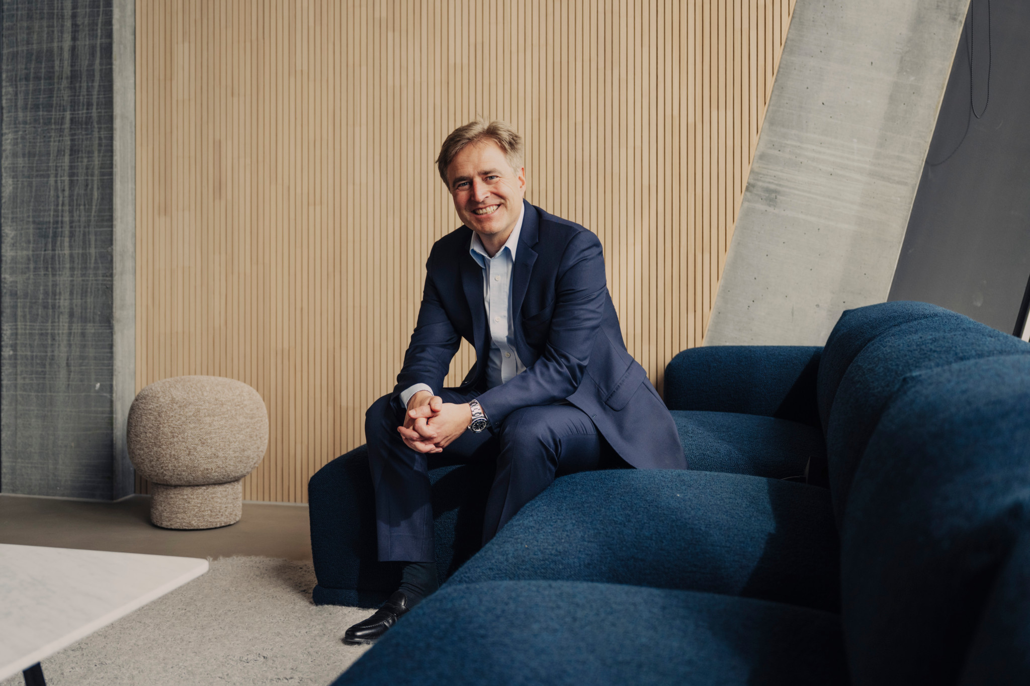 Fabian Rupprecht, CEO du groupe Helvetia Baloise, assis sur un canapé bleu au Circle de l’aéroport de Zurich, souriant en costume bleu marine.