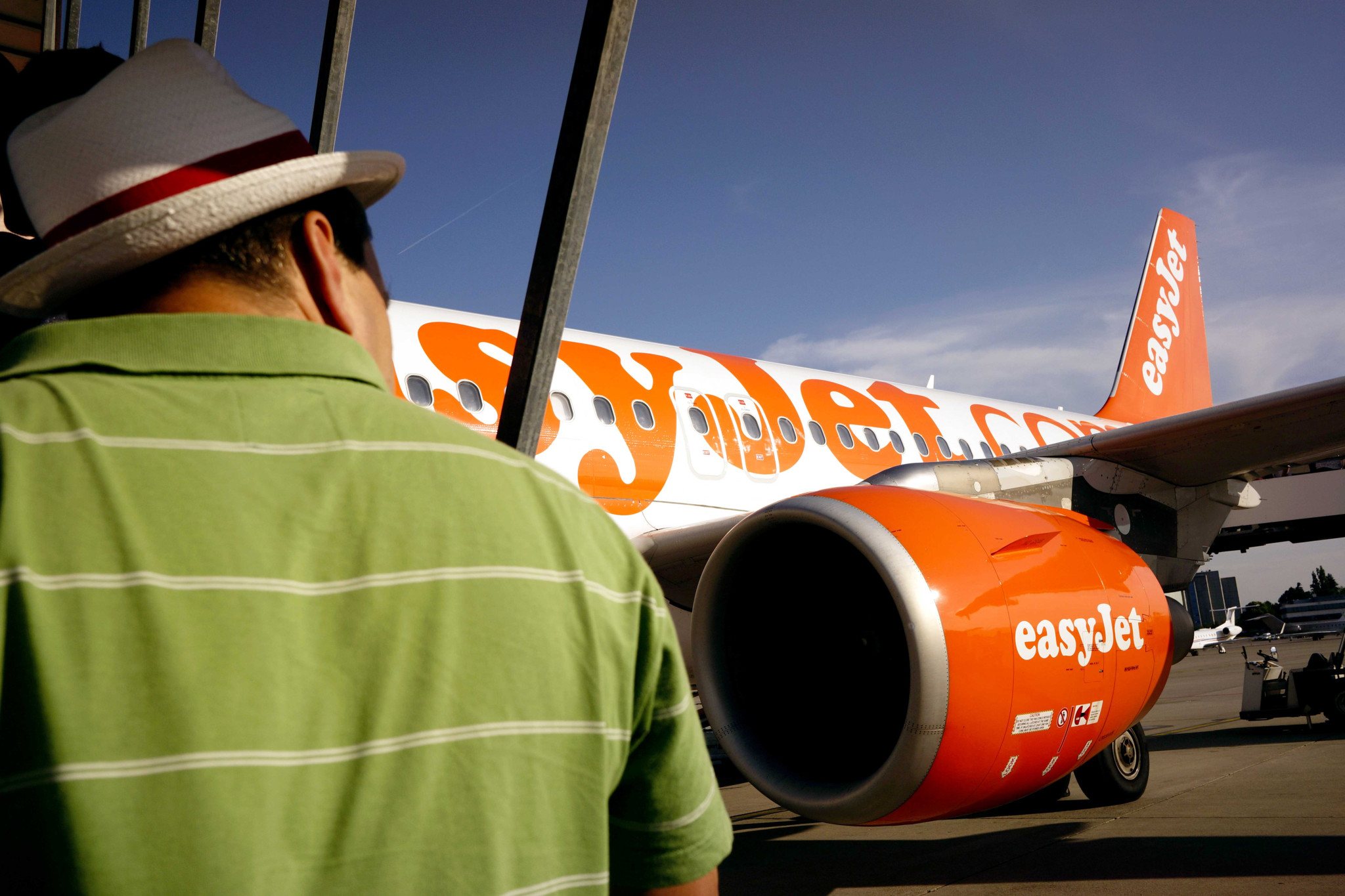Un passager observe un avion easyJet orange sur le tarmac de l’aéroport de Genève, moteur et logo visibles.