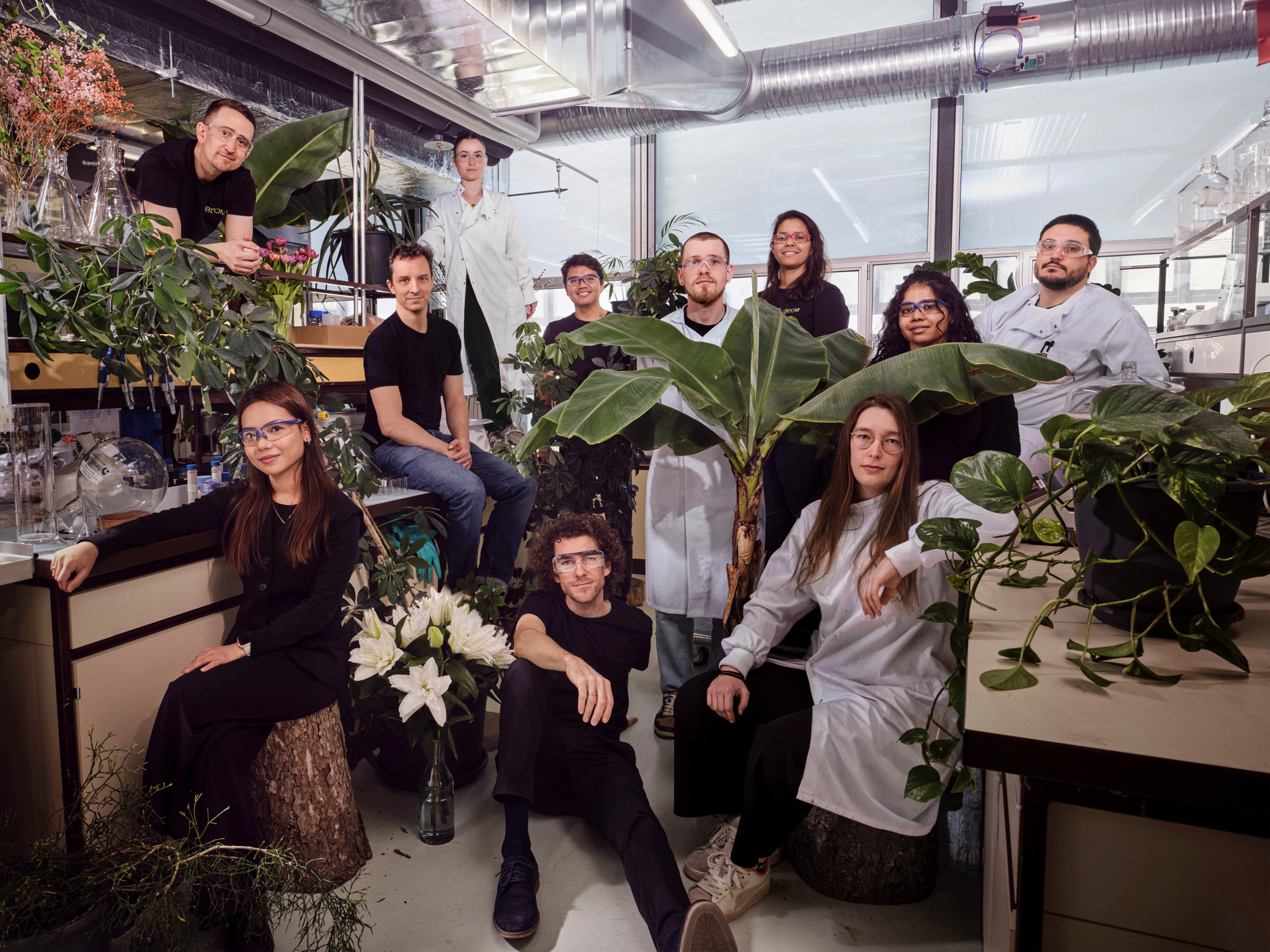 Groupe de personnes posant dans un laboratoire, entourées de plantes, y compris des lys blancs et diverses plantes vertes.