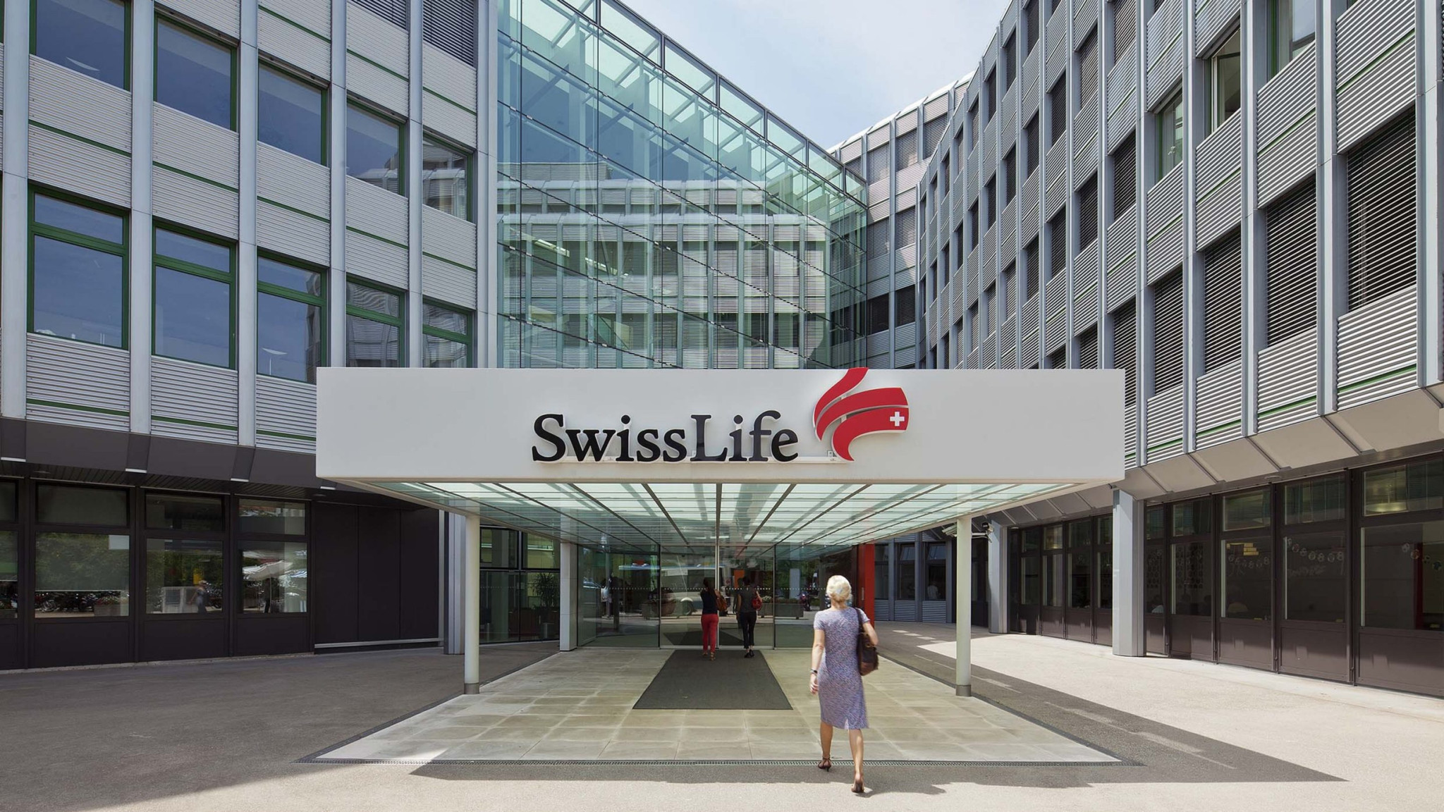Entrée du siège de Swiss Life avec une femme marchant vers le bâtiment moderne arborant le logo de l’assureur suisse