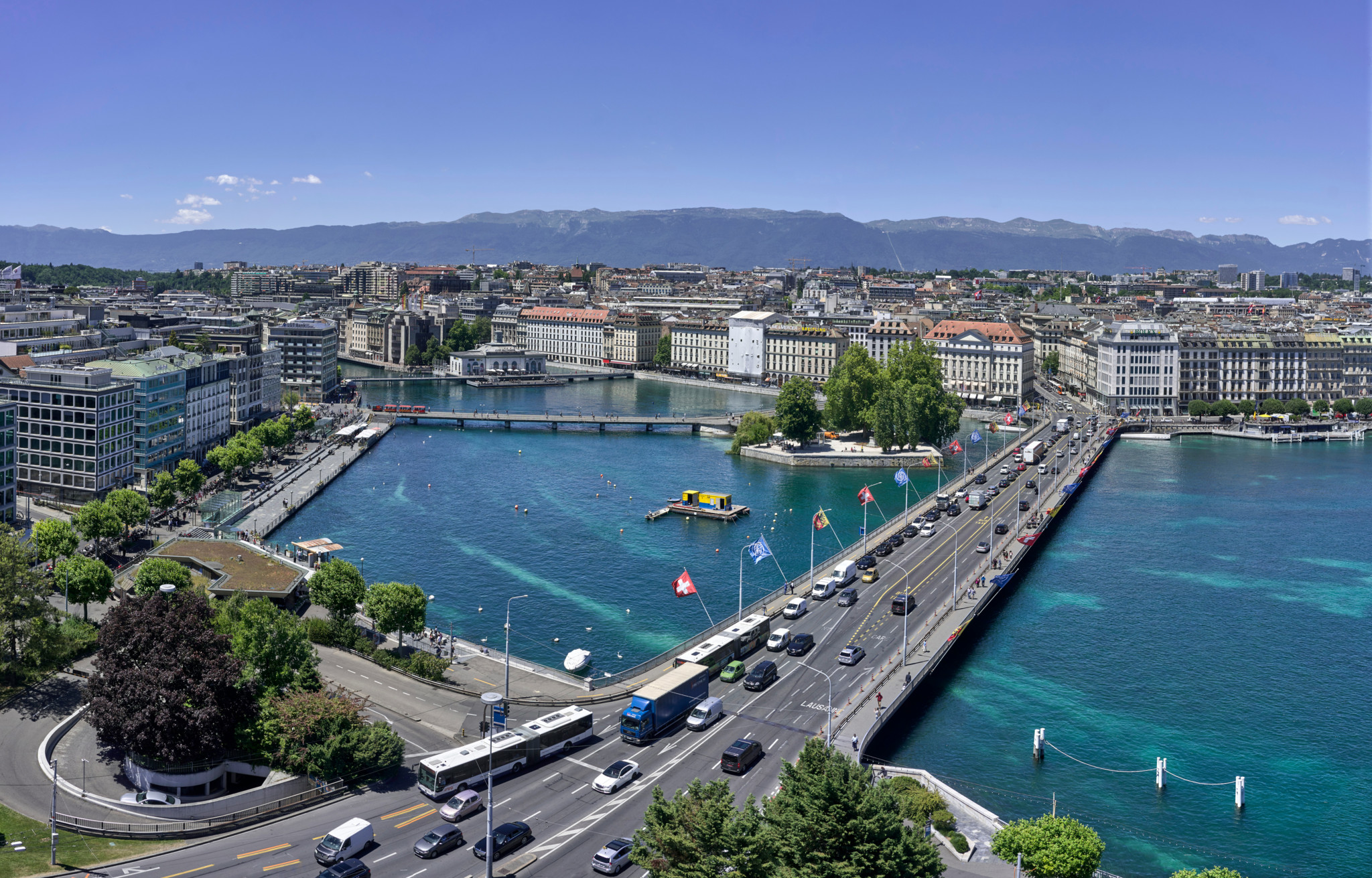 Vue aérienne de Genève avec le lac Léman aux eaux turquoise, le pont du Mont-Blanc et le centre-ville sous un ciel bleu estival.