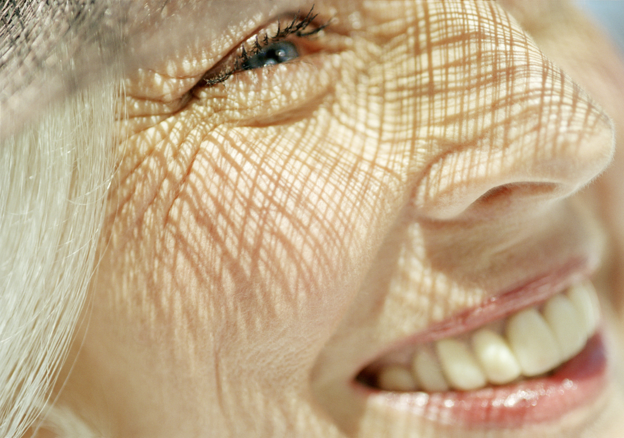 Gros plan sur le visage d’une femme âgée souriante aux cheveux blonds, mettant en évidence les rides et la texture de la peau