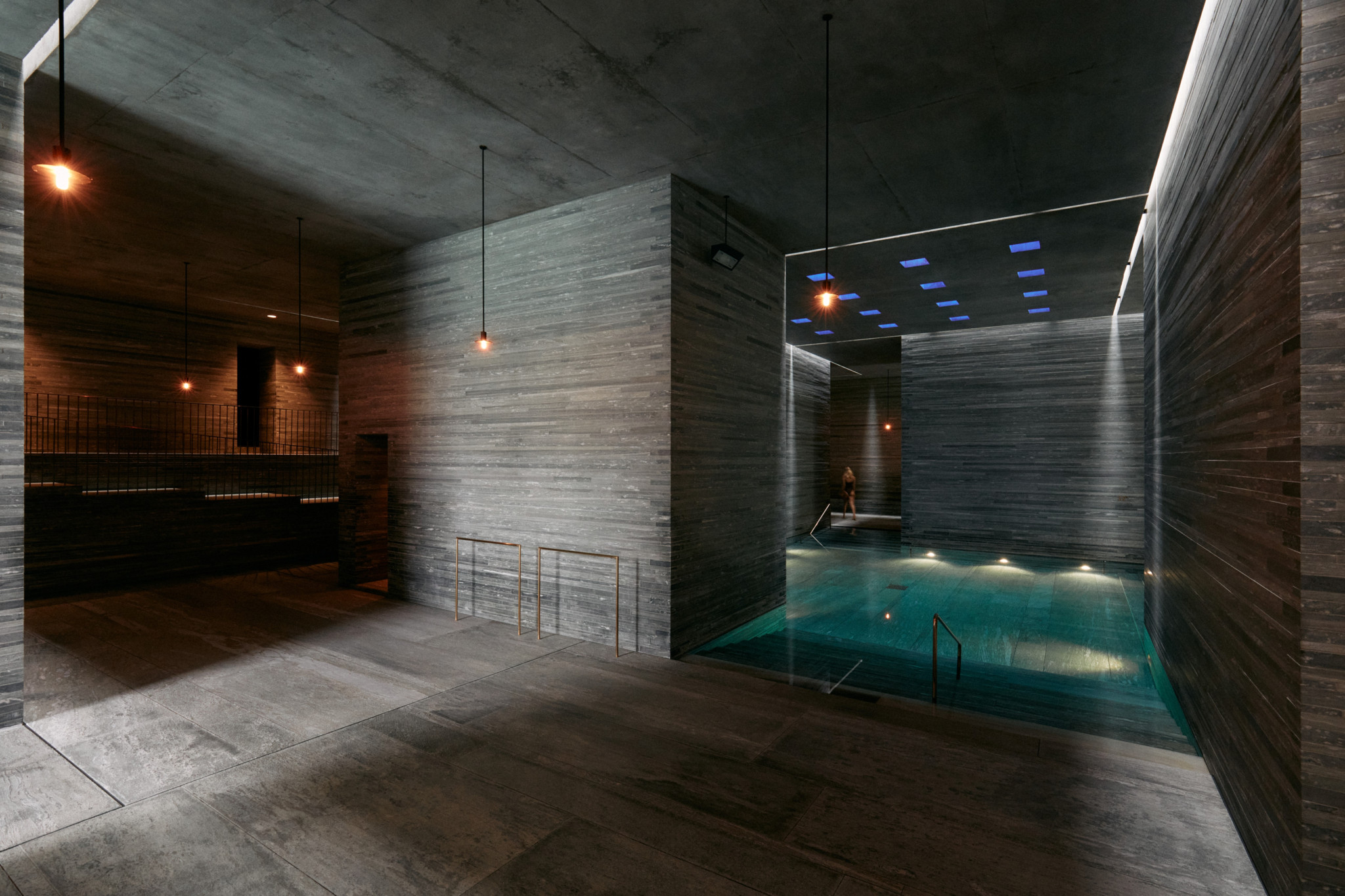 Espace spa intérieur luxueux avec piscine éclairée en turquoise, murs en béton brut et lumières bleues au plafond