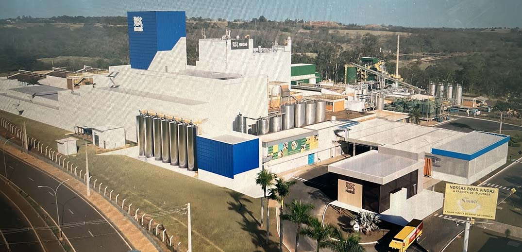 Vue aérienne d’un complexe industriel avec des bâtiments blancs et bleus, des silos métalliques et des installations de production entourées de verdure.