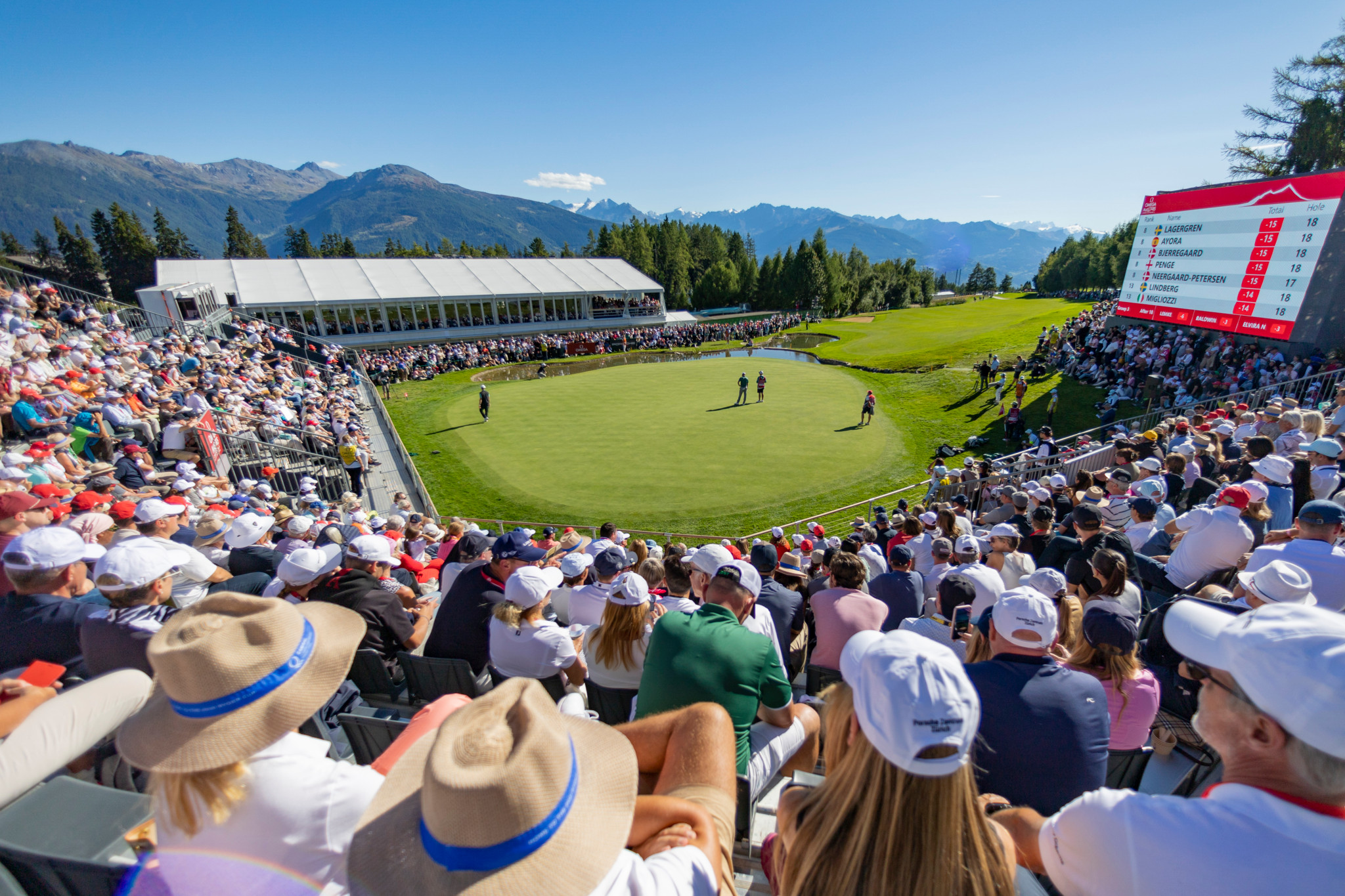 Tournoi de golf en plein air avec des spectateurs entourant le green, montagnes en arrière-plan, ciel bleu.